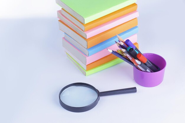 Magnifying glass pencils and stack of books on white background