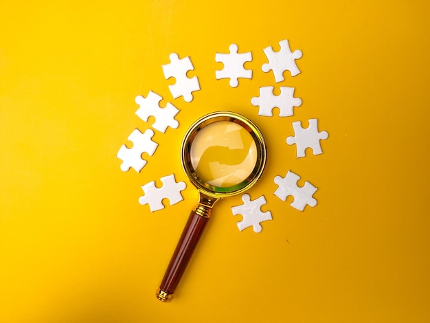 Magnifying glass searching missing puzzle on yellow background