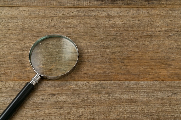 Photo a magnifying glass on shabby wooden board.