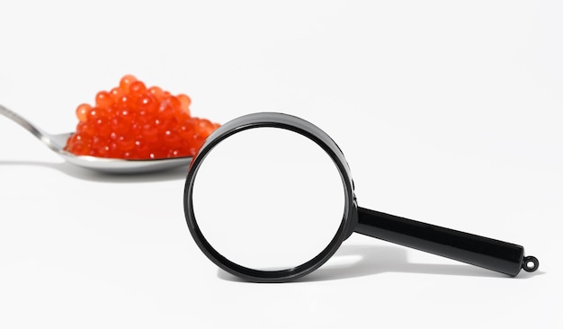 Magnifying glass and spoon with red caviar on a white background