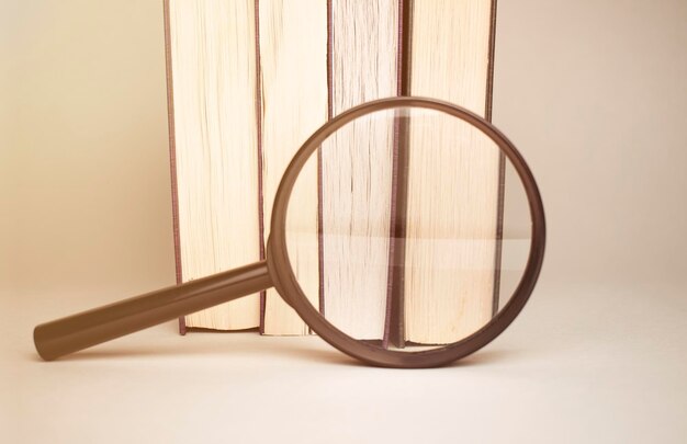 A magnifying glass on a stack of books on a blue wooden bookshelf with space for text