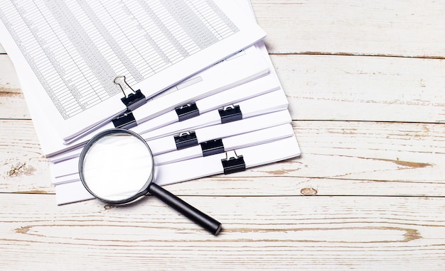 Photo a magnifying glass and a stack of documents lie on a light wooden table. business concept. copy space