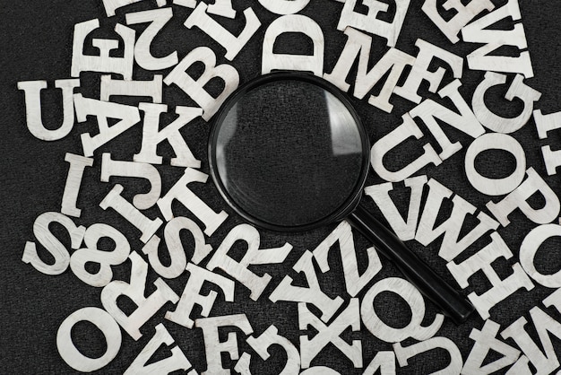 Photo magnifying glass surrounded by letters of english alphabet on black background. search words concept