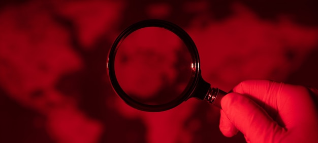 Magnifying glass on toned red  map, world pandemic concept