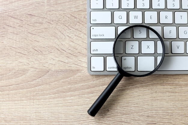 Magnifying glass on a white keyboard Web search and SEO concept