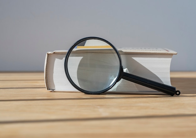 Foto lente d'ingrandimento con libro spesso vicino sul tavolo di legno con luce diurna