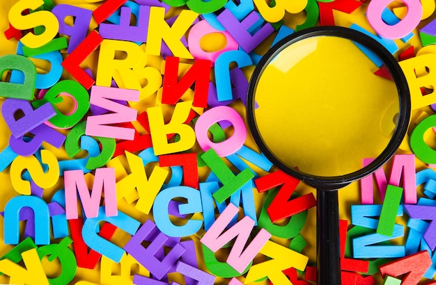 Magnifying glass with colorful alphabet on yellow backgroundeducation concept