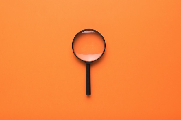 Magnifying glass with a handle on an orange background. Flat lay.