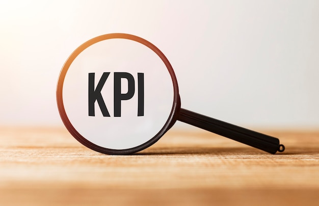 Magnifying glass with text KPI on wooden table.