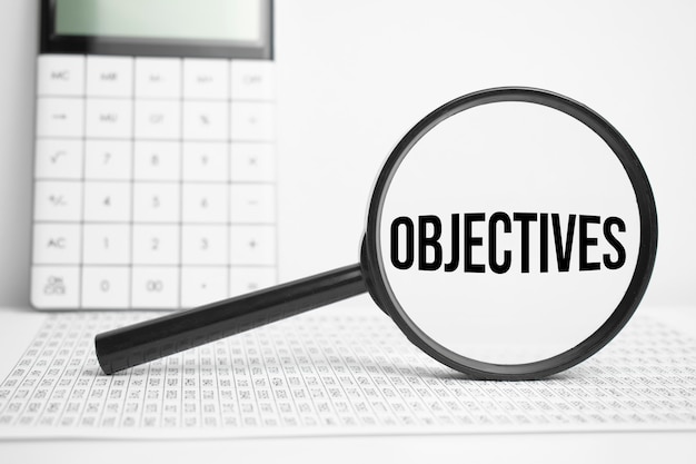 Magnifying glass with text Objectives on white table with calculator