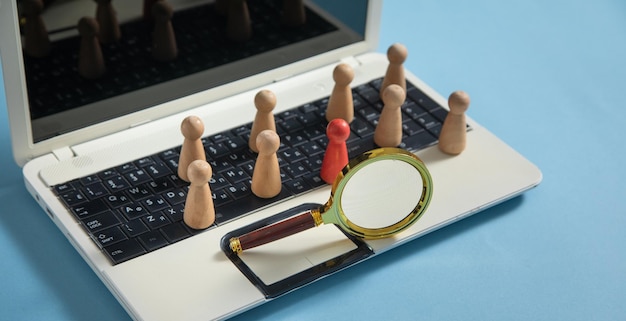 Magnifying glass wooden human figures on laptop keyboard Candidate selection