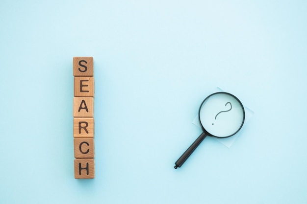 Magnifying glass and word search written wooden cubes on blue\
background search concept