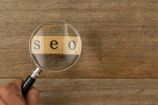 A magnifying glass and word Seo on shabby wooden board.