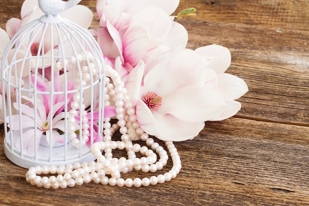 Magnolia bloemen met parels en vogelkooi op houten tafel