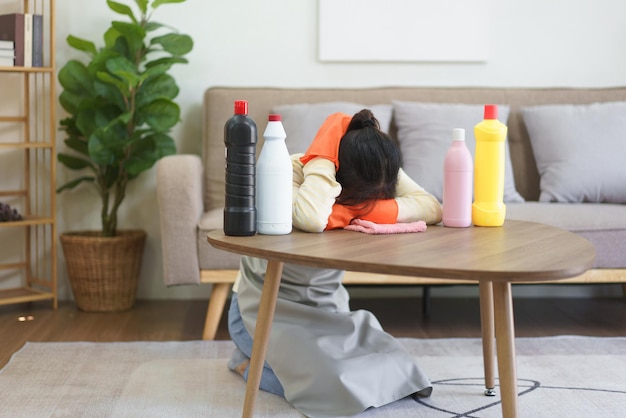 Photo maid exhausted and sleeping to resting on the table with cleansing bottles after cleaning in home