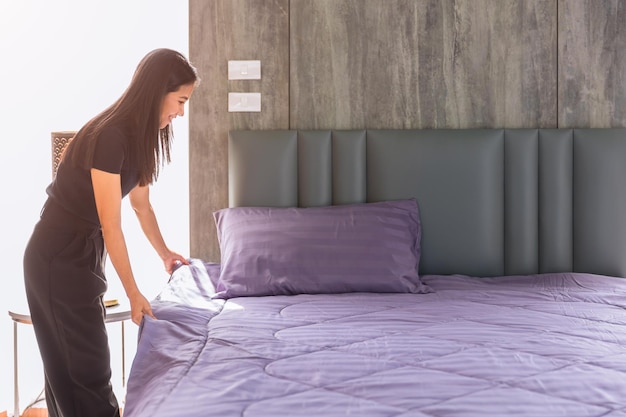 Maid housewife woman Preparing Bed pull tight neat bed sheet Lady working chores housekeeping cleaning bedroom at home or hotel
