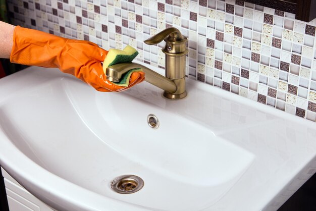 Maid is cleaning brass faucet in bathroom to remove limescale