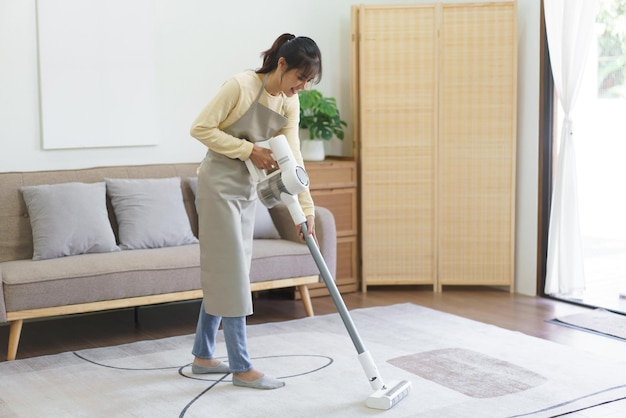 집에 있는 카펫의 먼지를 진공 청소기로 청소하고 청소하기 위해 무선 진공 청소기를 사용하는 가정부
