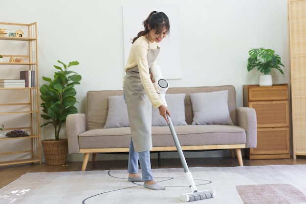 Maid using cordless vacuum cleaner to vacuuming and cleaning the dust on the carpet in home