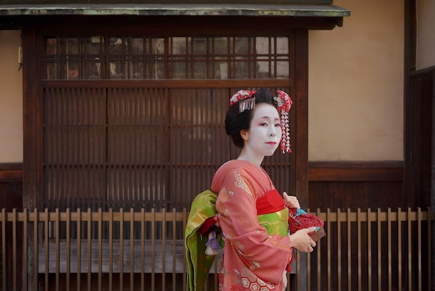 Maiko in een kimono loopt voor de poort van een traditioneel Japans huis in Kyoto