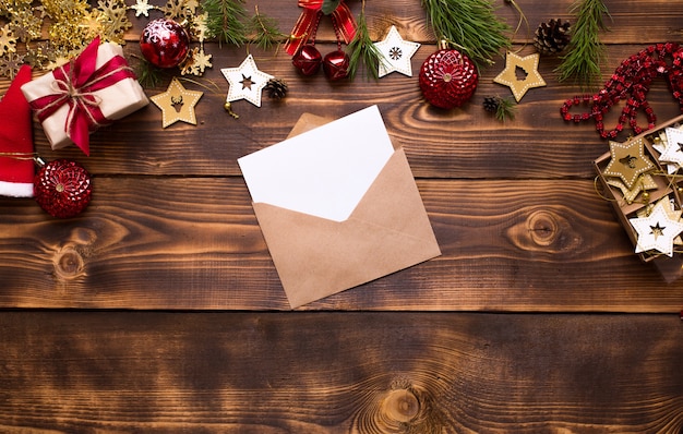 Busta per posta fatta di carta artigianale con un foglio bianco per il testo su uno sfondo di legno con decorazioni natalizie. una lettera a babbo natale, una lista dei desideri, il sogno di un nuovo anno, un regalo. lay piatto, copia dello spazio