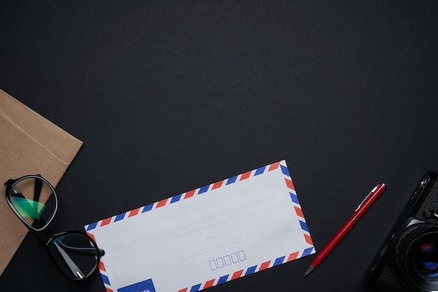 Mail envelope , pen,glasses and camera on black background . Top view .