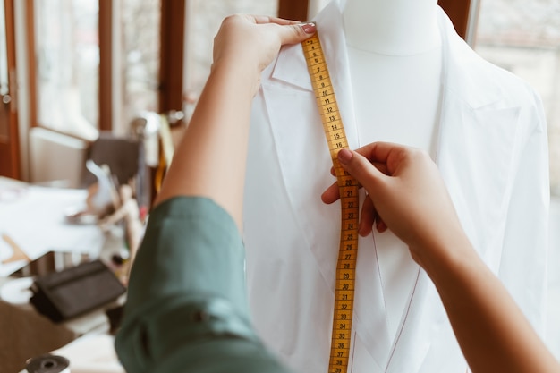 La cosa principale è la taglia giusta. il progettista della donna sta misurando la camicia bianca con nastro adesivo, primo piano