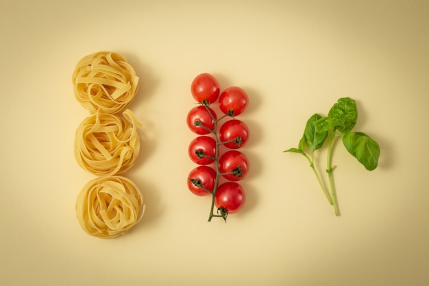 イタリア料理の主な伝統的な食材：パスタタリアテッレ、チェリートマト、新鮮なグリーンバジル。イタリア料理の最小限の料理のコンセプト、明るい黄色のパステルカラーの背景。上面図、フラットレイ