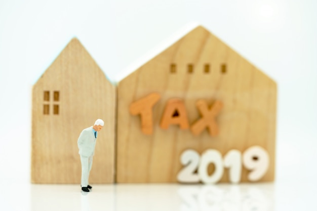 Mainature people standing with home and wording TAX 2019.