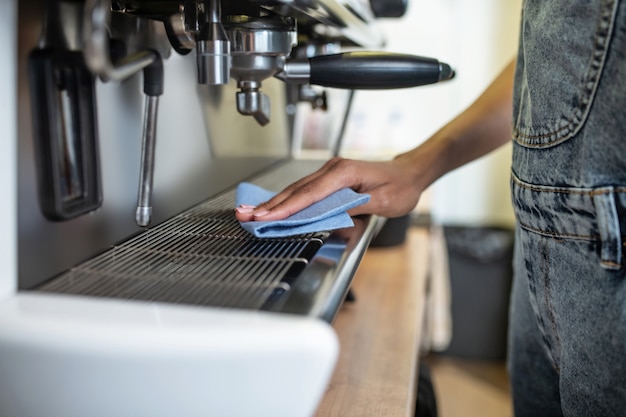 Mantenere la pulizia. mano femminile che lava la superficie della macchina da caffè che tocca il tovagliolo nel posto di lavoro del caffè