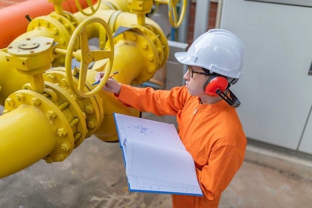 Foto tecnico di manutenzione in un impianto di riscaldamento lavoratori petrochimici supervisionano il funzionamento dei gasdotti e dei oleodotti in fabbrica gli ingegneri mettono la protezione dell'udito in una stanza con molti tubi