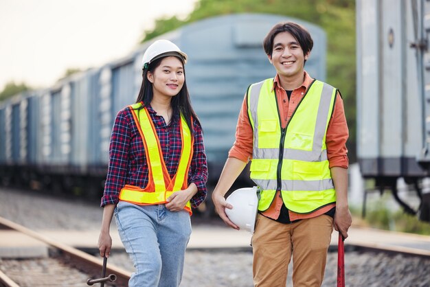 Il tecnico di manutenzione in una tuta di sicurezza si trova accanto a un treno merci con la chiave inglese. i lavoratori asiatici lavorano nell'industria del trasporto ferroviario. ingegnere e concetto di riparazione. la sicurezza prima