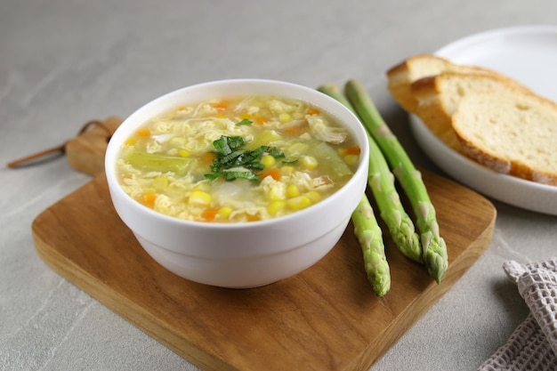 Maïs en asperges met eierdruppelsoep in witte kom en krokant brood