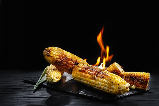 Maïskolf op de grill met rook en vlammen tegen een zwarte achtergrond een vegetarische barbecue boven een ca