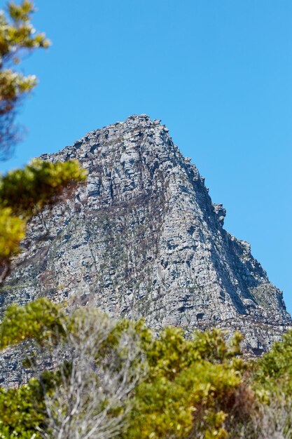 澄んだ青い空と下からコピースペースで隔離された雄大な山頂風光明媚で静かな山頂または晴れた夏の日の遠隔地の岩の多い風景の景色を望む頂上