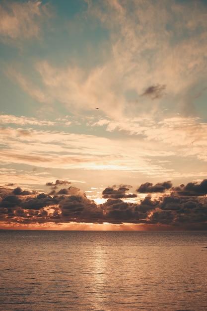 Majestic sun flares coming through the clouds during a sunset over the ocean on orange tones and with copy space