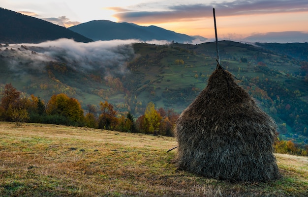 Majestic sunrise in misty morning valley with haystack on grassland hill