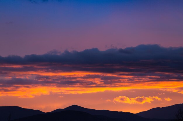 Величественный яркий закат с облаками над силуэтами темных гор