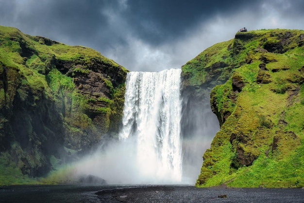 Majestueuze Skogafoss waterval stroomt met regenboog en humeurige lucht in de zomer in IJsland