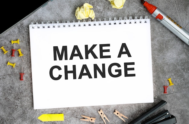 Make a change text on a white notebook with pins, marker and stapler on a concrete table