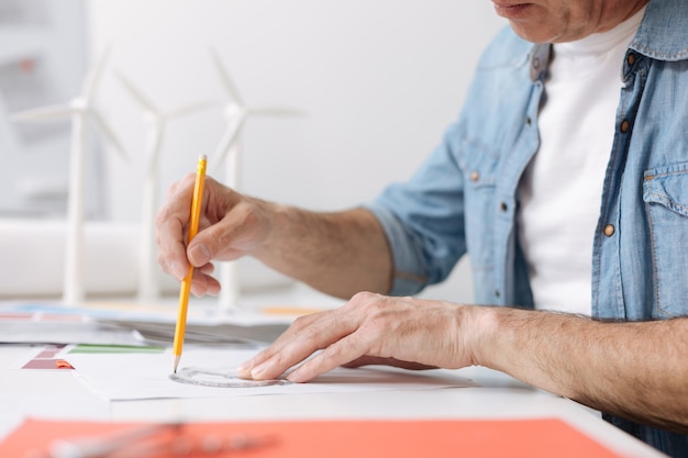 Make everything correctly. Professional skillful engineer sitting at the table and using a protractor while drawing a blueprint