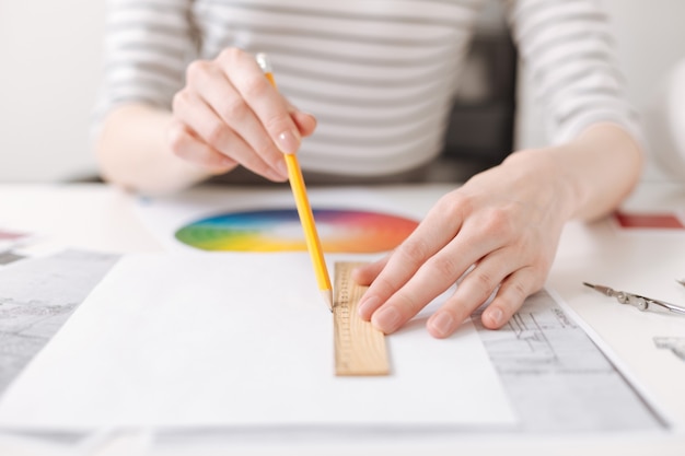 Make it straight. Close up of a ruler in hands of professional skillful female engineer drawing and working on the project in the office