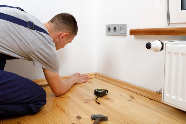 To make repairs Installing a new skirting board a man makes repairs in a room