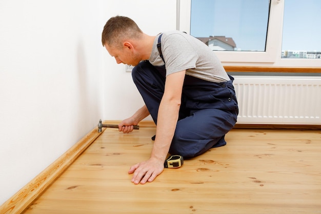 To make repairs Installing a new skirting board a man makes repairs in a room