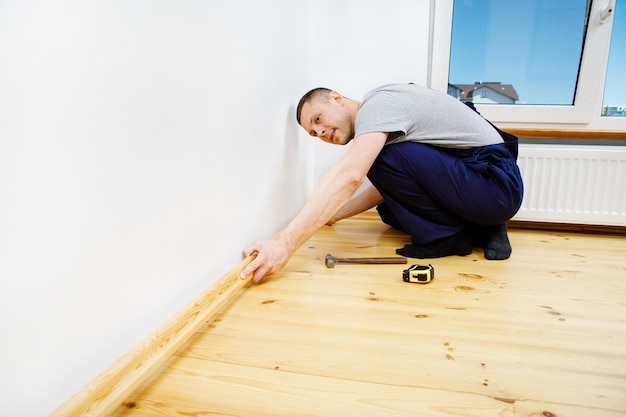 To make repairs Installing a new skirting board a man makes repairs in a room