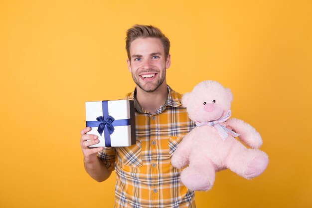 Make surprise concept. Cute and romantic. Bearded hipster play toy yellow background. Birthday boy. Positive vibes. Cute teddy bear toy. Softness tenderness. Valentines day gift. Man hug soft toy.