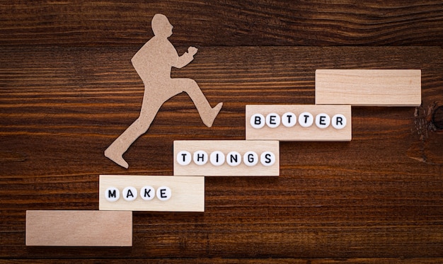 Make things better - improvement concept. paper man climbing the steps to success in a conceptual image over wooden background.