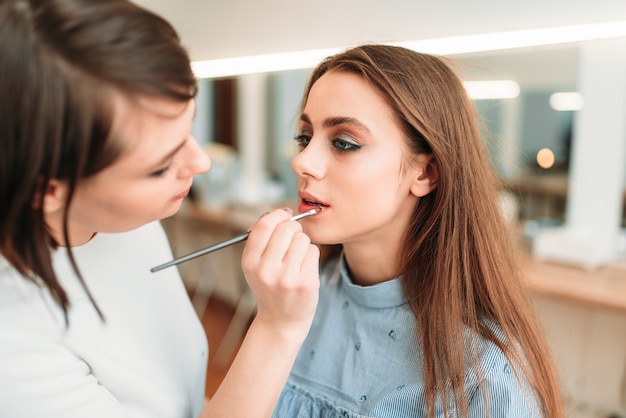 Make-up artiest hand glans toe te passen op de lippen van de vrouw