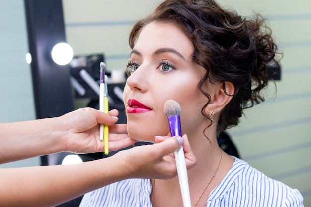 Make up artist applies a light layer of matte powder using a professional makeup brush. girl at makeup artist