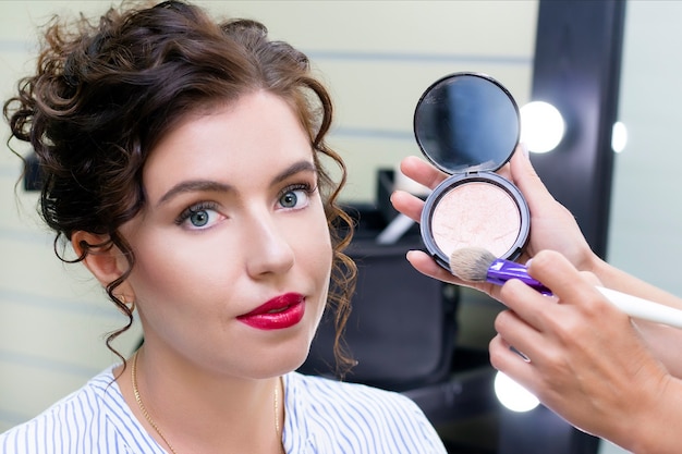 Photo make up artist applies a light layer of matte powder using a professional makeup brush. girl at makeup artist